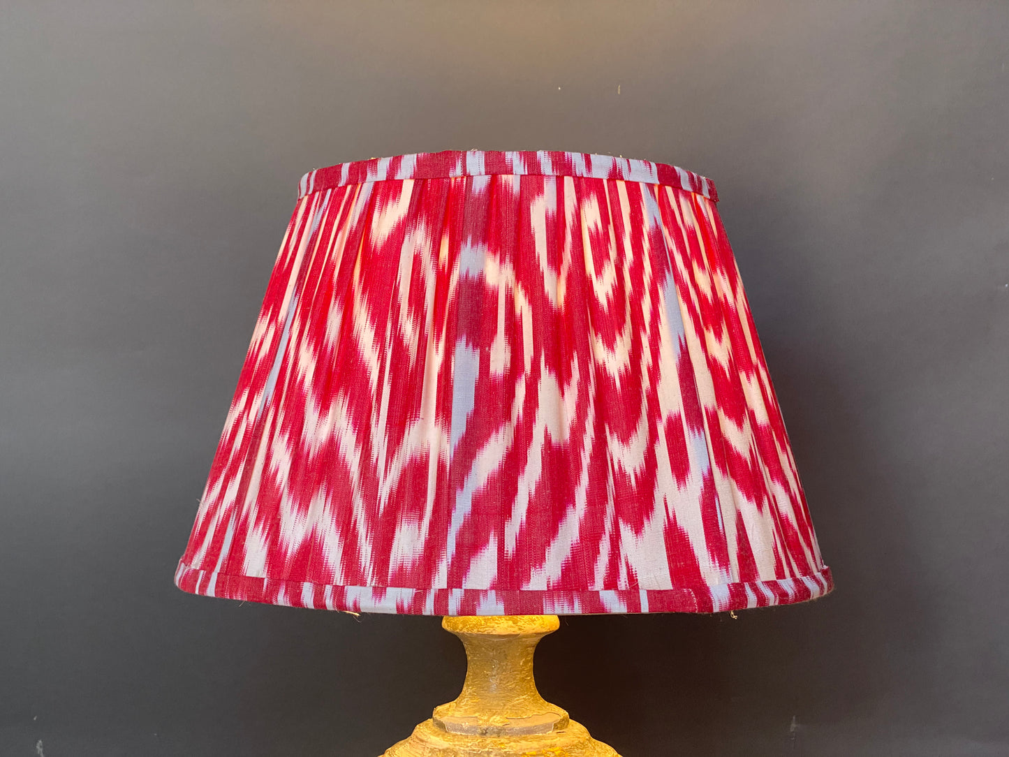 Red and white ikat silk lampshade shown lit on a grey background