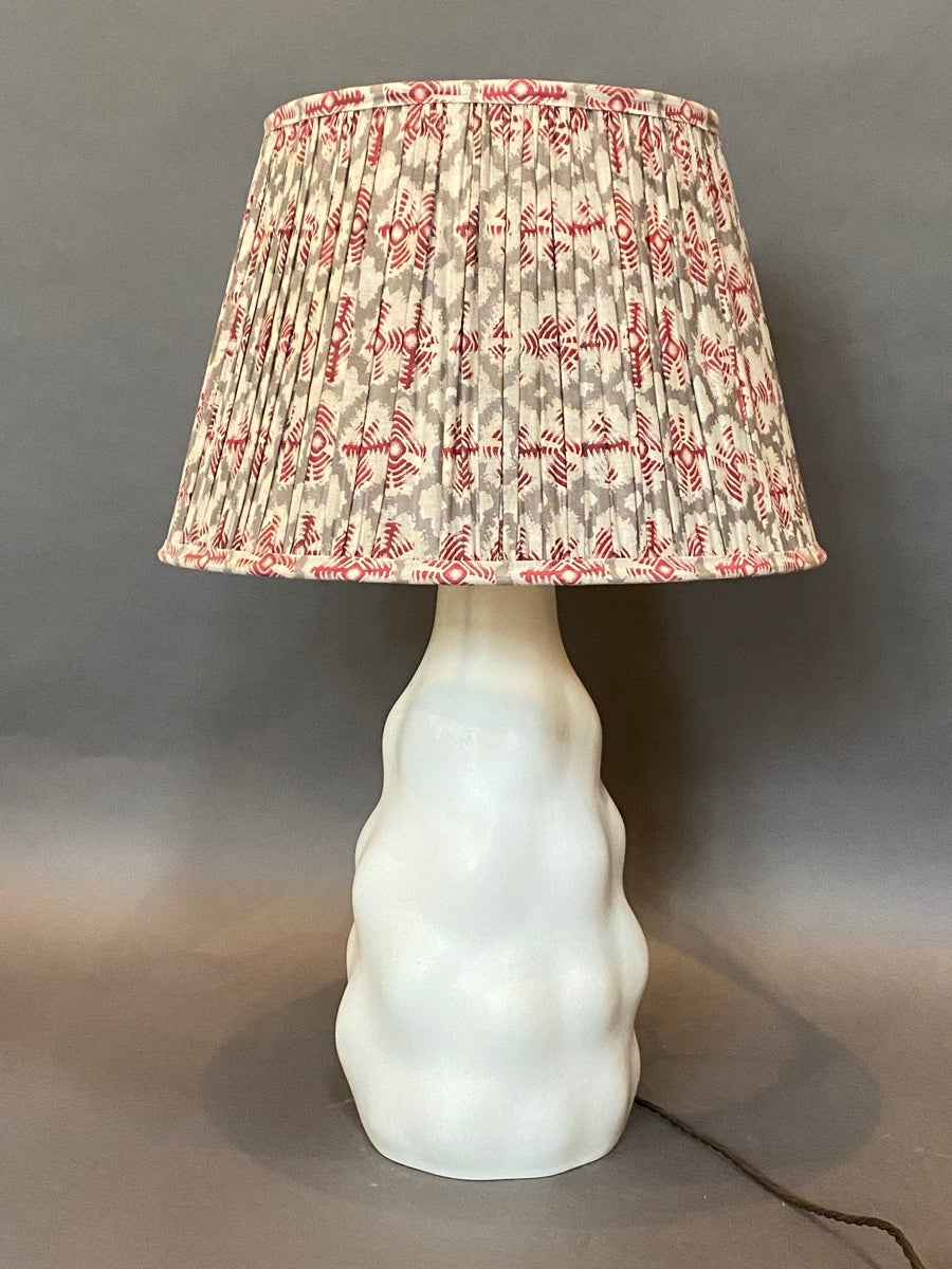 Red cotton lampshade shown on a ceramic base on a grey background